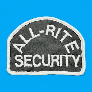 May include: Black and white embroidered patch with the text "ALL-RITE SECURITY" in a white arched font on a black background.