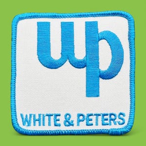May include: A white embroidered patch with blue stitching. The patch features the letters "wp" in a stylized font and the text "WHITE & PETERS" below.