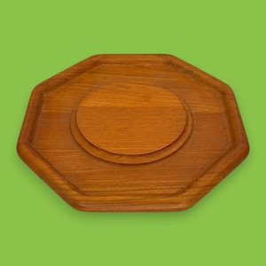 May include: A wooden serving tray with an octagonal shape and a circular recessed area in the center. The tray is made of a light brown wood and has a smooth, polished finish. The tray is designed for serving food or drinks.