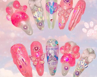 May include: A set of ten pink and white nail charms with various designs, including butterflies, paw prints, and a bunny with the text "My cuteness is my curse".