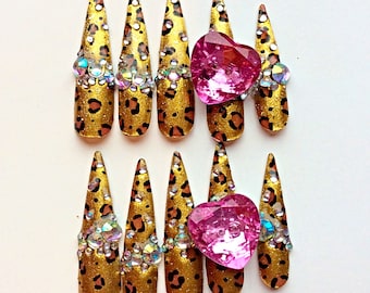 May include: Set of ten false nails with a leopard print design. Each nail has a clear rhinestone accent and a pink heart-shaped rhinestone at the top.