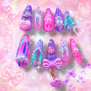 Könnte beinhalten: Set mit 10 bunten, glitzernden und verzierten falschen Nägeln mit einem rosa Schleifen-Anhänger. Die Nägel sind in verschiedenen Schattierungen von Rosa, Lila und Blau mit Glitzer- und Perlenakzenten.