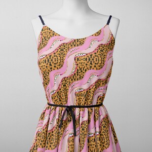 May include: A sleeveless dress with a pink and brown leopard print pattern. The dress has a black ribbon tie at the waist.