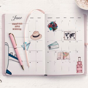 May include: A pink open planner with a monthly calendar layout for June. The planner has a pink pen, a paper airplane, a hat, a camera, a world map, a plane ticket, a map, and a suitcase drawn on it. The planner has the words "Travel the World" written on it.