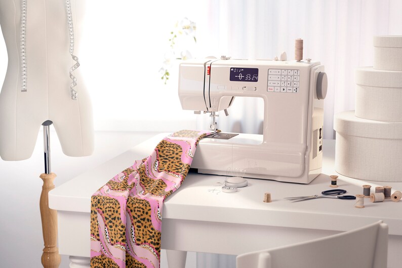 May include: A white sewing machine with a digital display showing "0-0 35.24". The machine is on a white table with a pink and brown leopard print fabric, spools of thread, and a pair of scissors.