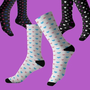 Puede incluir: Varios pares de calcetines altos con patrones de corazones. Los calcetines son negros y blancos, con corazones rosas, azules y morados. Los calcetines tienen talones y dedos negros. El fondo es morado.