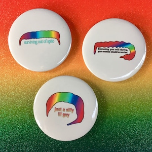 May include: Three round white button pins with rainbow worm illustrations and text. The first pin says "surviving out of spite". The second pin says "Someday you will thrive, your enemies should be worried.". The third pin says "just a silly lil guy".