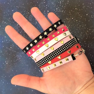 May include: A stack of seven colorful bracelets with different designs. The bracelets are made of faux leather and feature gold stars, hearts, and studs.