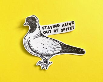 May include: A sticker featuring a black and white illustration of a pigeon with the text "STAYING ALIVE OUT OF SPITE!" on a white banner. The sticker is set against a bright yellow background.