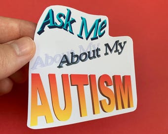 May include: A white sticker with the text "Ask Me About My AUTISM" in blue, orange, and yellow. The sticker is held against a red background.