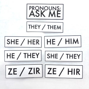 May include: A set of eight white rectangular cards with black borders and text. The cards display various pronoun sets, including "They/Them", "She/Her", "He/Him", "He/They", "She/They", "Ze/Zir", and "Ze/Hir". The top card reads "Pronouns: Ask Me".
