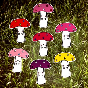 Peut inclure: Sept autocollants en forme de champignon colorés avec des étoiles blanches et des visages souriants. Les champignons sont rouges, roses, violets, jaunes et de différentes nuances de rouge.