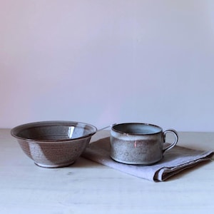 Pode incluir: Um conjunto de três canecas de cerâmica com esmalte salpicado creme. Cada caneca apresenta um design pintado à mão diferente: uma folha azul e verde, uma flor amarela e uma baga vermelha. As canecas têm uma forma simples e arredondada.