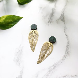 May include: A pair of gold leaf-shaped earrings with green and black patterned round accents.
