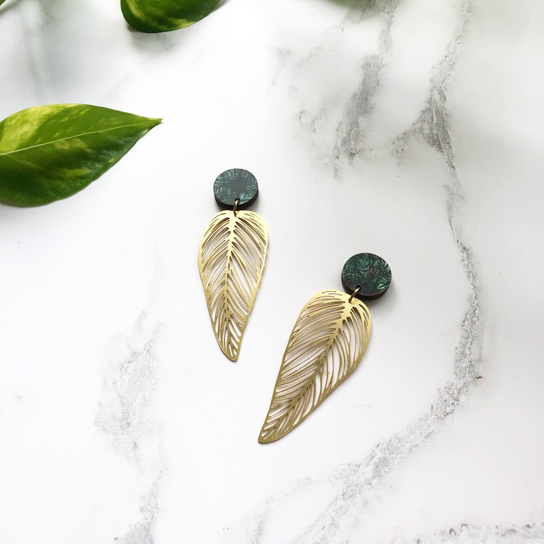 May include: A pair of gold leaf-shaped earrings with green and black patterned round accents.