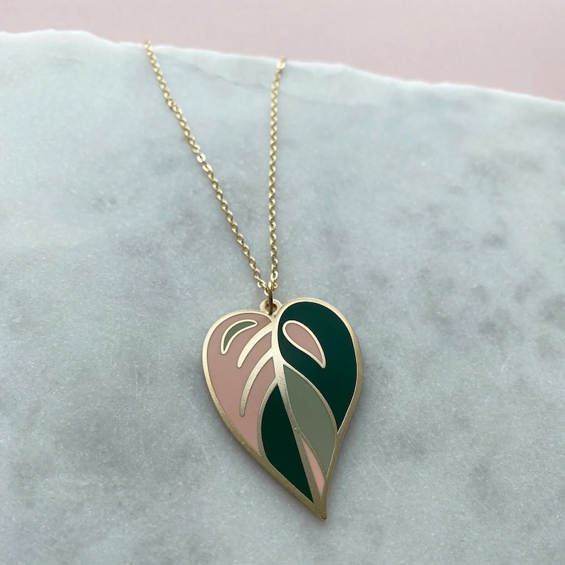 May include: A gold chain necklace with a heart-shaped pendant. The pendant is made of gold metal and is painted with pink, green, and gray enamel. The pendant is shaped like a leaf.