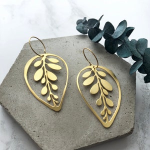 May include: A pair of gold leaf-shaped earrings with a delicate cutout design. The earrings are made of brass and have a simple hoop closure.