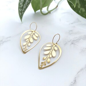May include: A pair of gold leaf-shaped earrings with a delicate cutout design. The earrings are made of metal and have a simple, elegant style.