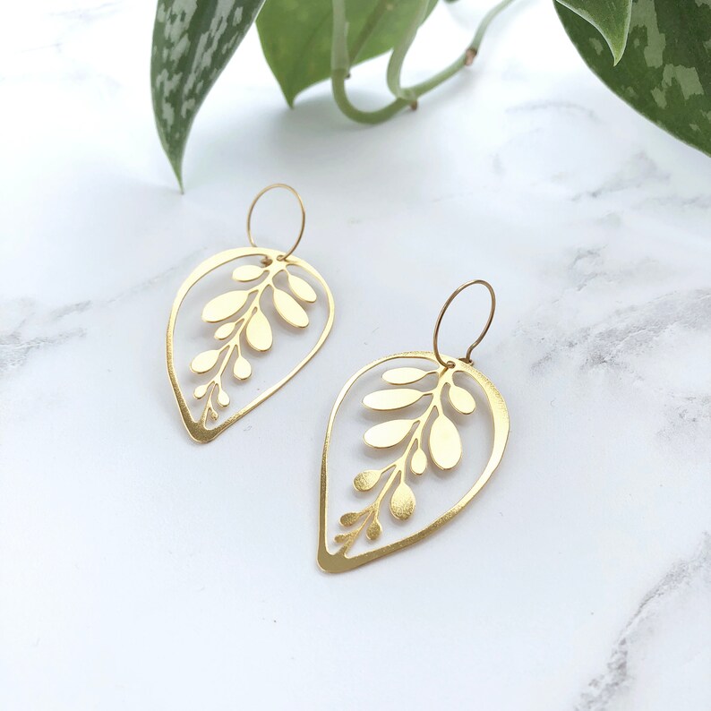 May include: A pair of gold leaf-shaped earrings with a delicate cutout design. The earrings are made of metal and have a simple, elegant style.