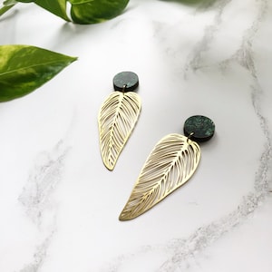May include: A pair of gold leaf earrings with green and black marbled accents. The earrings are made of metal and have a delicate, intricate design.