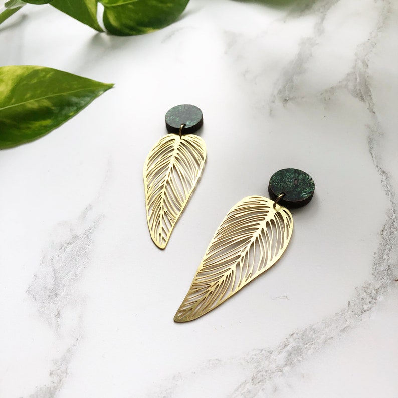 May include: A pair of gold leaf earrings with green and black marbled accents. The earrings are made of metal and have a delicate, intricate design.