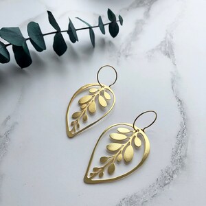 May include: A pair of gold leaf-shaped earrings with a delicate cutout design. The earrings are made of brass and have a simple, elegant style.