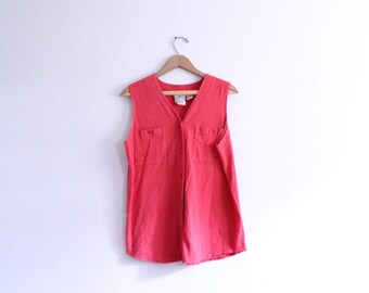 May include: A sleeveless, button-up shirt in a bright coral colour. The shirt has two pockets on the front and a V-neck.