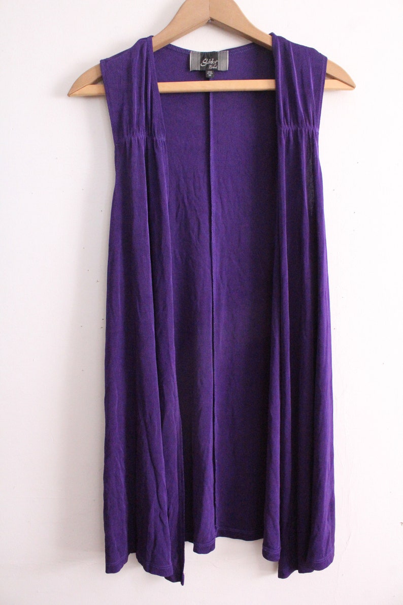 Puede incluir: Un c&aacute;rdigan morado sin mangas con un dise&ntilde;o largo y fluido. El c&aacute;rdigan tiene un estilo simple y elegante y est&aacute; hecho de una tela suave y c&oacute;moda.