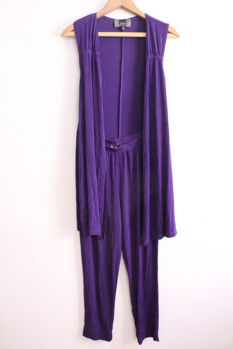 Puede incluir: Un conjunto de dos piezas morado con una chaqueta sin mangas y pantalones a juego. La chaqueta tiene un dise&ntilde;o drapeado y los pantalones tienen una pierna recta.