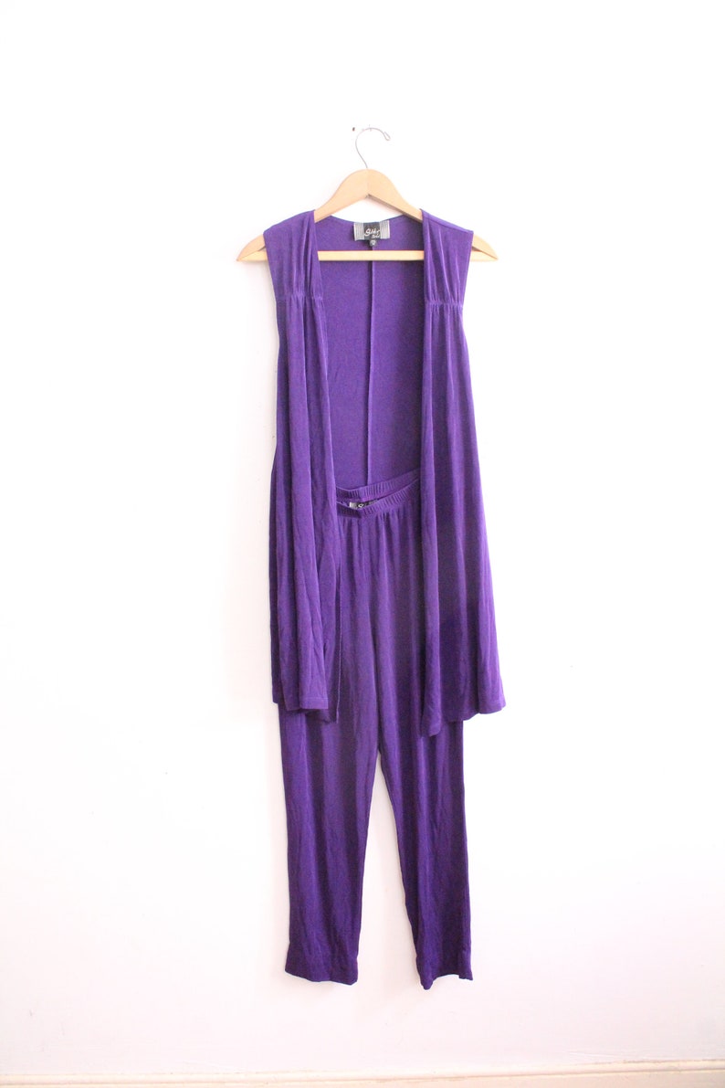 Puede incluir: Un conjunto de dos piezas morado con un c&aacute;rdigan sin mangas y pantalones a juego. El c&aacute;rdigan tiene un frente drapeado y los pantalones tienen una pierna recta.