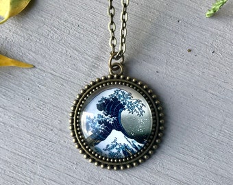 May include: A bronze necklace with a round pendant featuring a depiction of The Great Wave off Kanagawa by Katsushika Hokusai. The pendant has a beaded border.