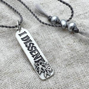 Silver necklace with 'DISSENT' pendant on a textured fabric background