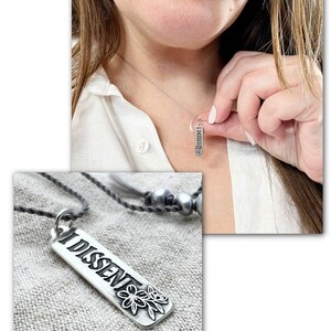 Person wearing a silver necklace with 'DISSENT' pendant, close-up of necklace on white background.
