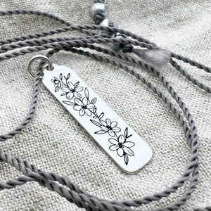 Silver necklace with a floral pendant on a textured fabric background
