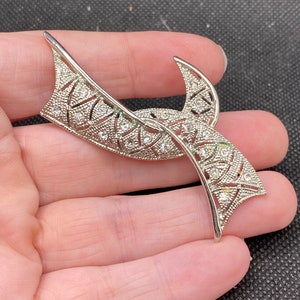 May include: Silver tone brooch with a geometric design and clear rhinestones.