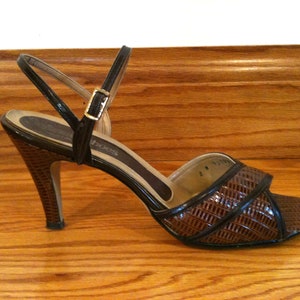 May include: A brown and black leather heeled sandal with a woven design. The sandal has a buckle closure and a high heel.