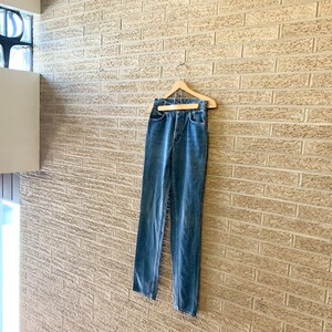 May include: A pair of blue denim jeans hanging on a wooden hanger against a brick wall.