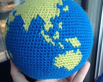 May include: A crocheted globe with blue and yellow yarn. The continents are outlined in yellow yarn.