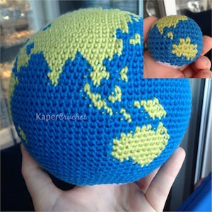 Puede incluir: Un globo terráqueo de crochet con hilo azul y verde, que representa la Tierra. El globo se sostiene en una mano, y el texto "KaperCrochet" es visible en el globo.