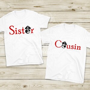 Two white t-shirts with red text that says "Sister" and "Cousin" printed on them, laid out on a wooden surface.
