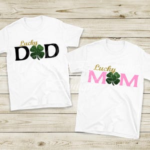 two white t-shirts with the text "Lucky Dad" and "Lucky Mom" printed on them, along with a green clover symbol.