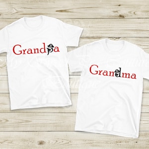 Two white t-shirts with the text "Grandpa" and "Grandma" printed on them, placed on a wooden surface.