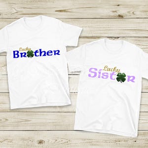 Two white t-shirts with the text "Lucky Brother" and "Lucky Sister" printed on them, along with a clover leaf symbol.