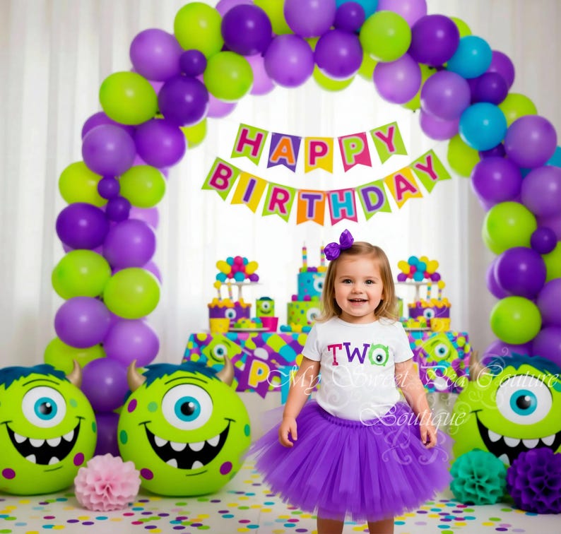 A young girl in a purple tutu and a "Happy Birthday" banner stands in front of a colorful balloon arch, with two monster-themed balloons on either side.