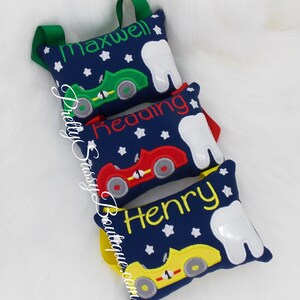 May include: Three blue tooth fairy pillows with white teeth, each with a different colored race car and a name embroidered on the pillow: Maxwell, Reading, and Henry.