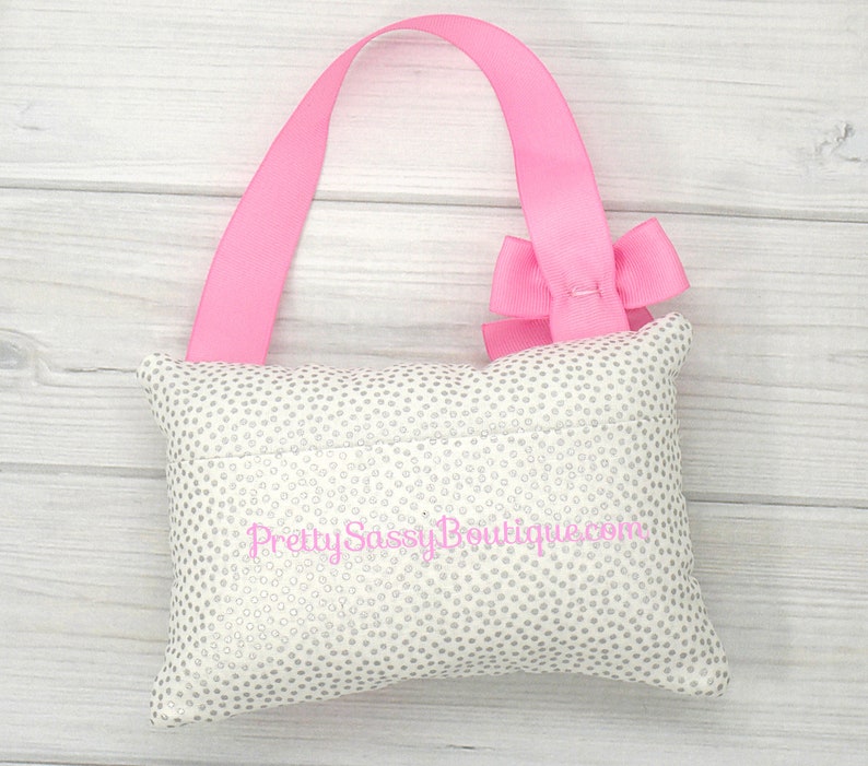May include: A white pillow with silver glitter dots and a pink ribbon bow. The pillow has a pink ribbon loop for hanging and the text "Pretty Sassy Boutique.com" is embroidered on the front.