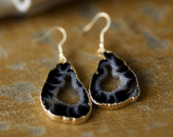 May include: A pair of gold-plated drop earrings featuring a black and white geode design. The earrings have a teardrop shape with a gold border and a hook closure. The geode pattern has a unique, natural appearance.