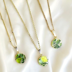 May include: Three gold necklaces with green and gold pendants. Each pendant is a round, flat disc with a unique pattern of green and gold.