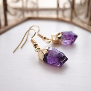 May include: A pair of gold earrings with amethyst crystal drops. The crystals are raw and have a natural, irregular shape.