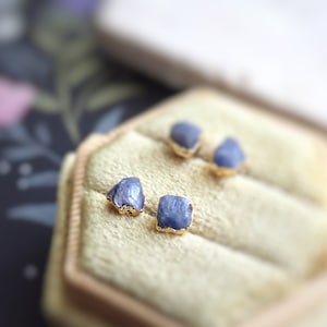 May include: Four blue gemstone earrings in a velvet ring box. The earrings are set in gold.